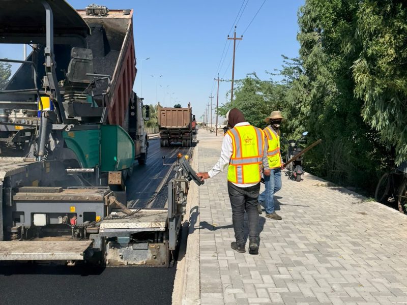 Paving alongside the completed interlock sidewalk and curb — full street cross-section.