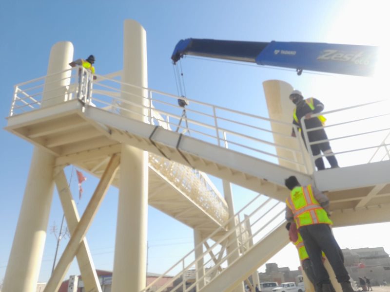 Fall-protected Al Shamsh crew installing the staircase platform at height, supported by a Tadano mobile crane.