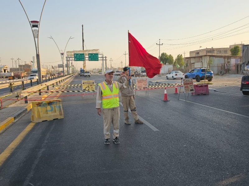 Traffic-management crew with warning flag and lane closure during deck-span installation.
